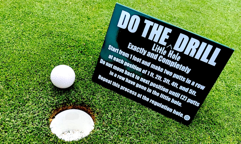 golf ball near cup with sign about the little hole drill